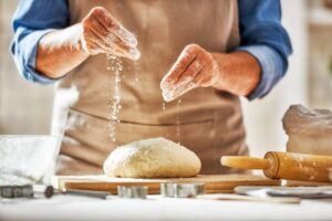 un homme mettant de la farine sur un pain pas encore cuit
