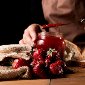 Personne se servant de la confiture de fraise avec des fraises au premier plan